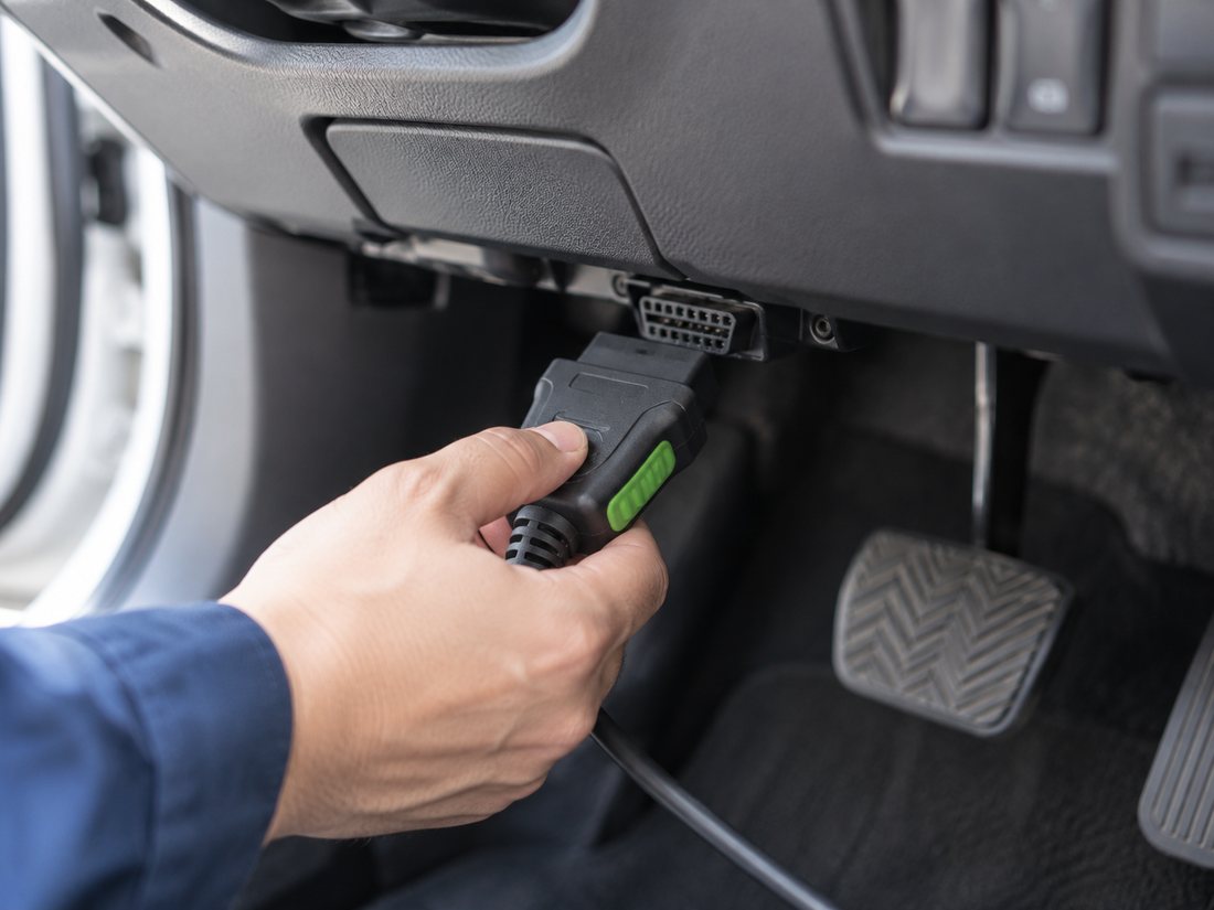 ハンドル下のOBD2コネクタに診断機のケーブルをつなぐ整備士の手元